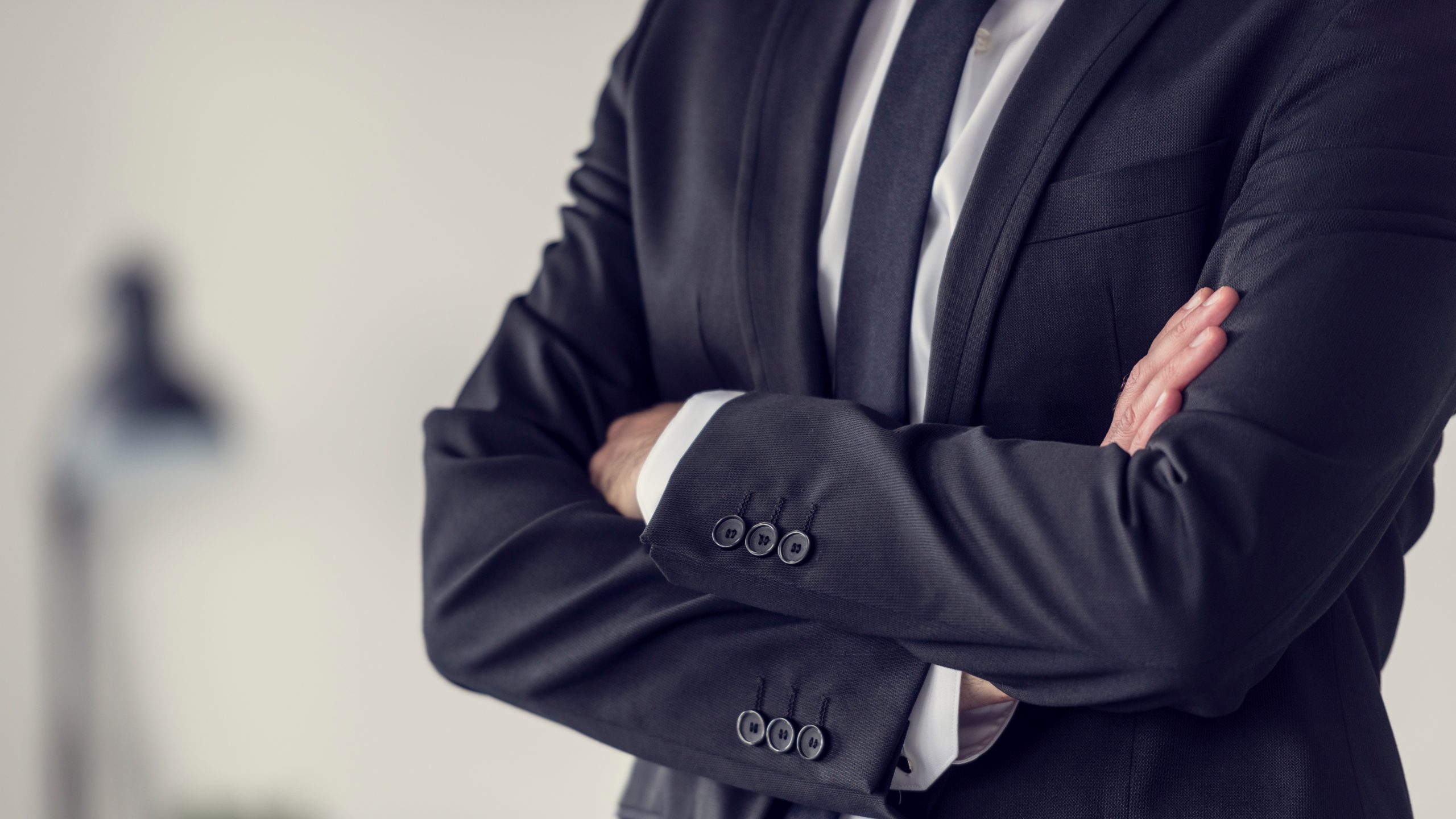 Torso of a businessman standing with folded arms in a classic black suit, toned retro effect.